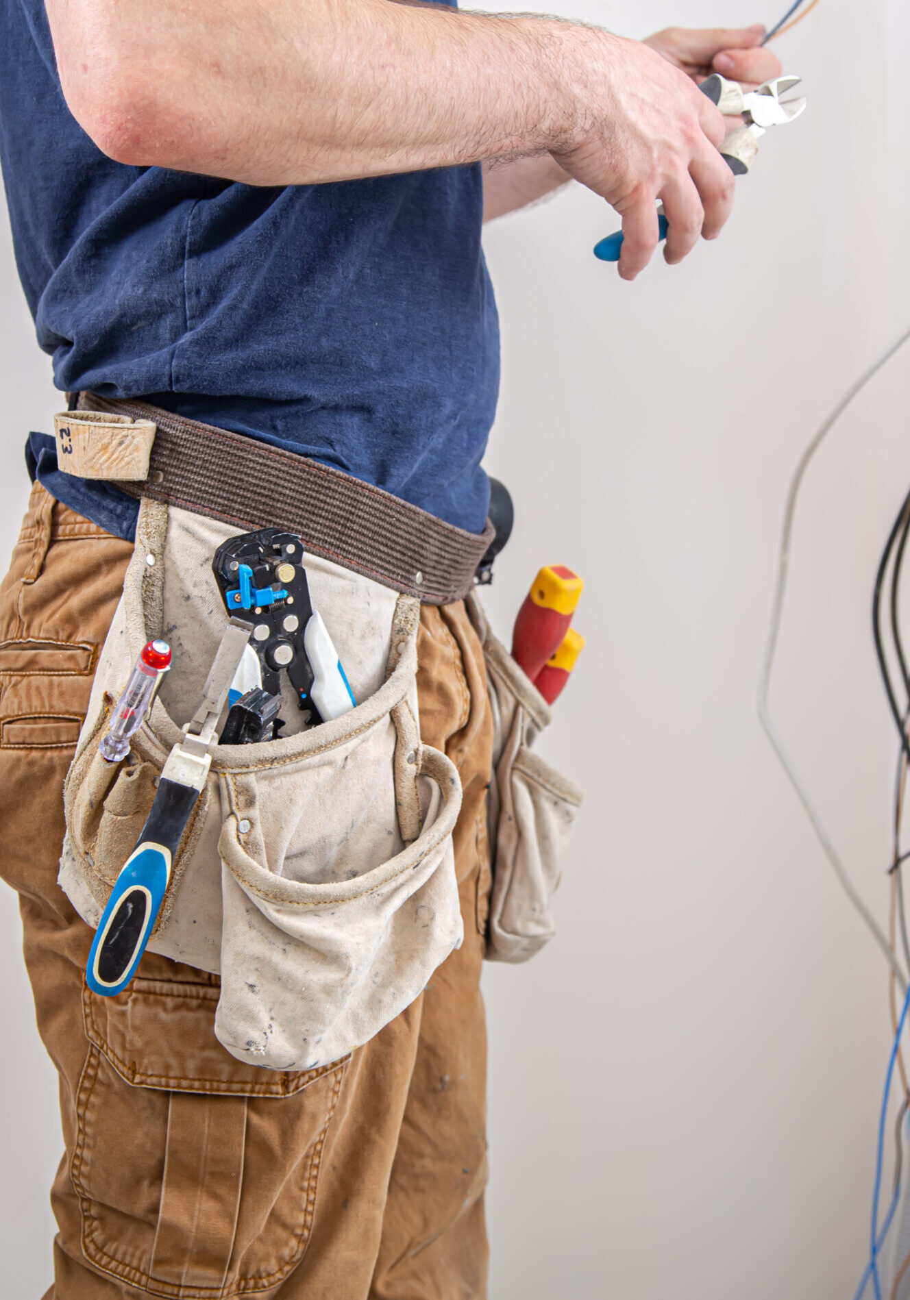 Electrician builder at work, examines the cable connection in the electrical line in the fuselage of an industrial switchboard. Professional in overalls with an electrician's tool.