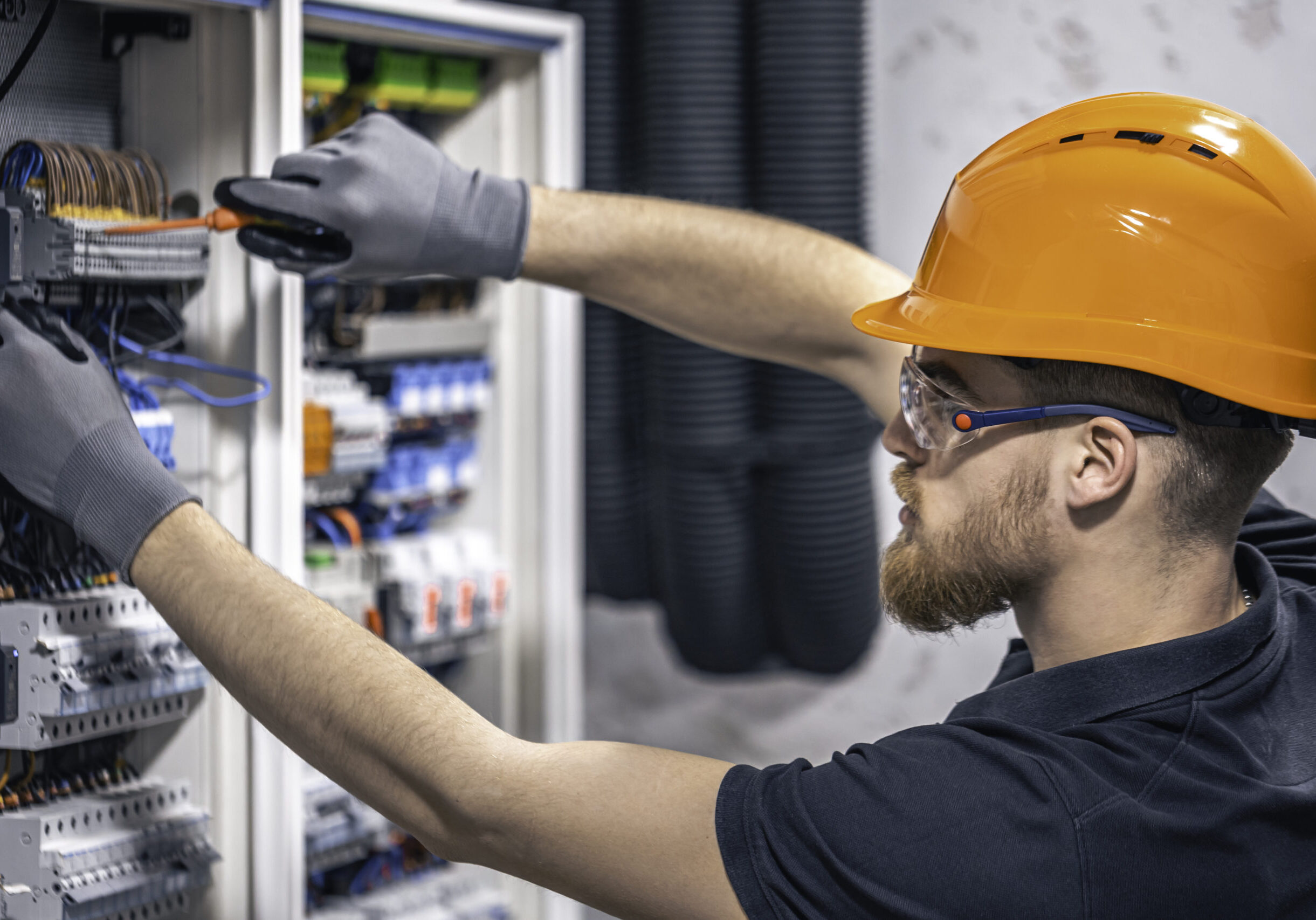 A male electrician works in a switchboard with an electrical connecting cable.