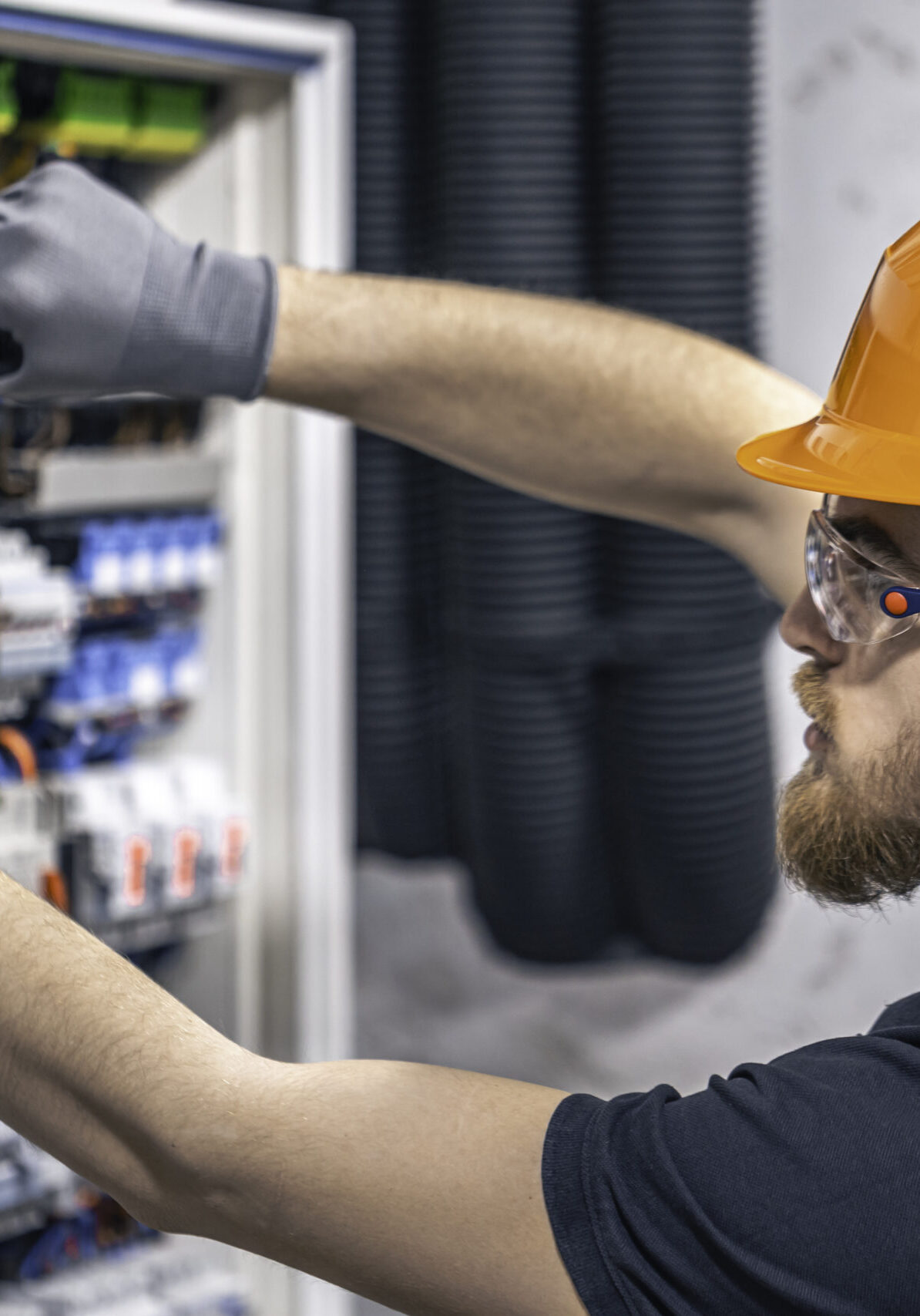 A male electrician works in a switchboard with an electrical connecting cable.