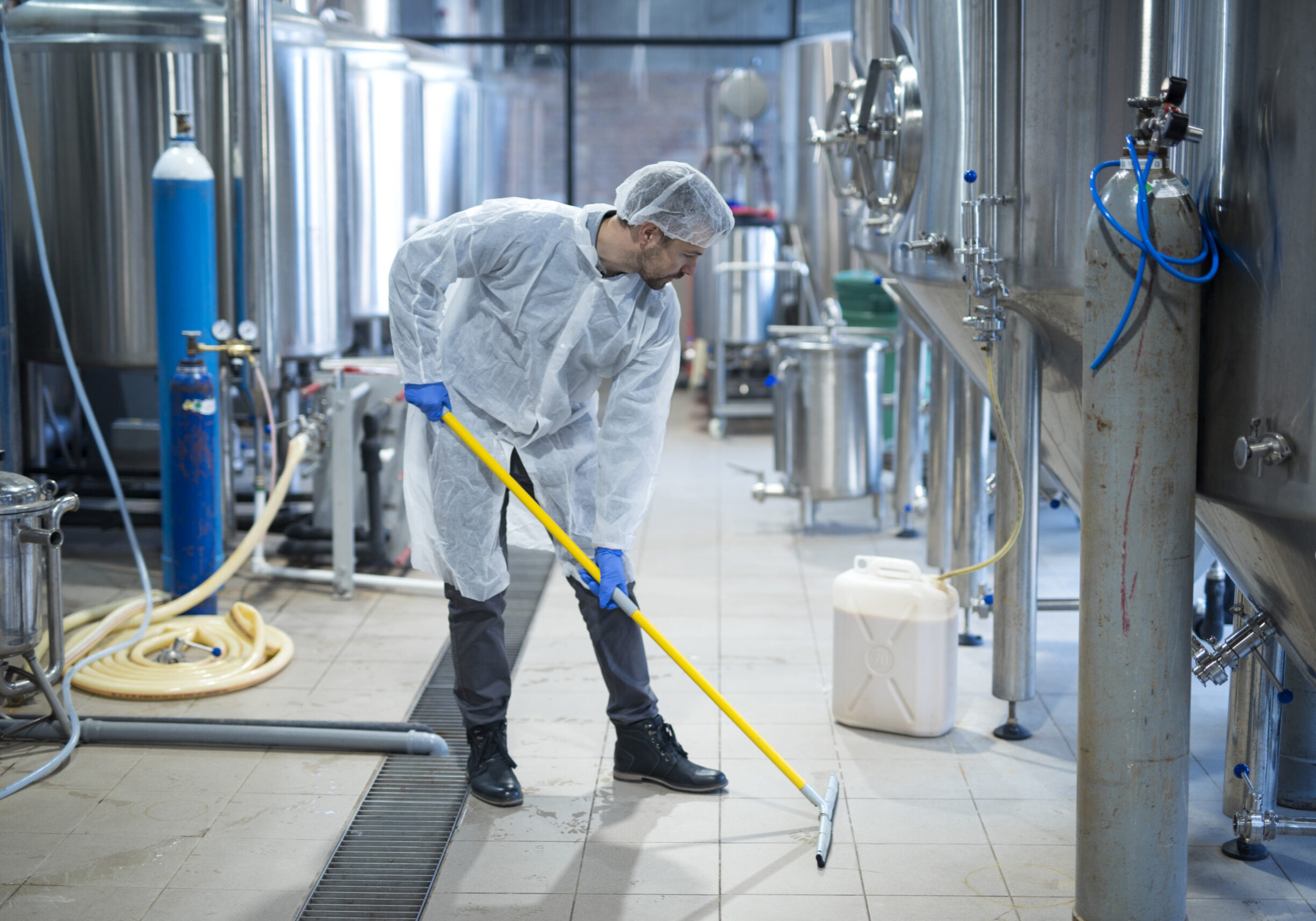 Professional industrial cleaner in protective uniform cleaning floor of food processing plant.