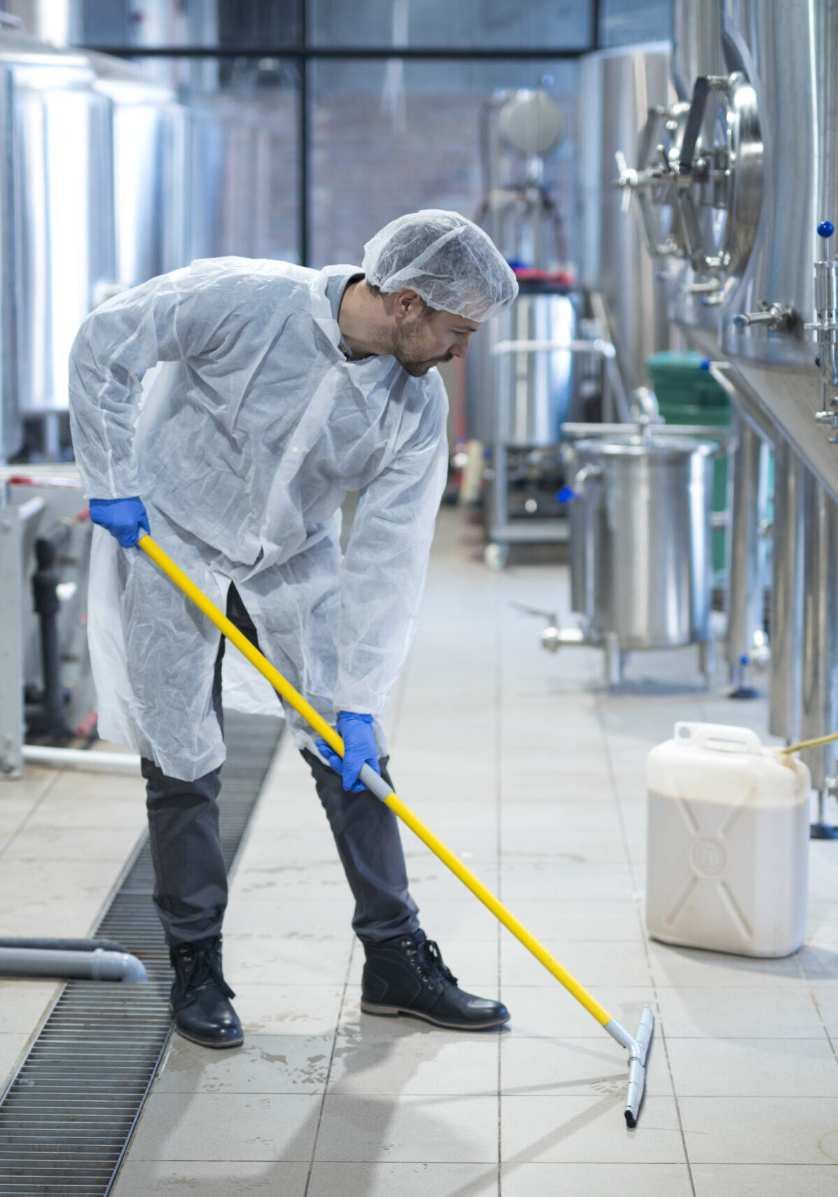 Professional industrial cleaner in protective uniform cleaning floor of food processing plant.